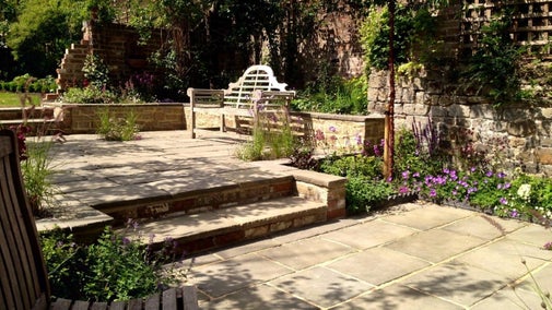 Split-level paved terraced garden with wooden bench on upper level