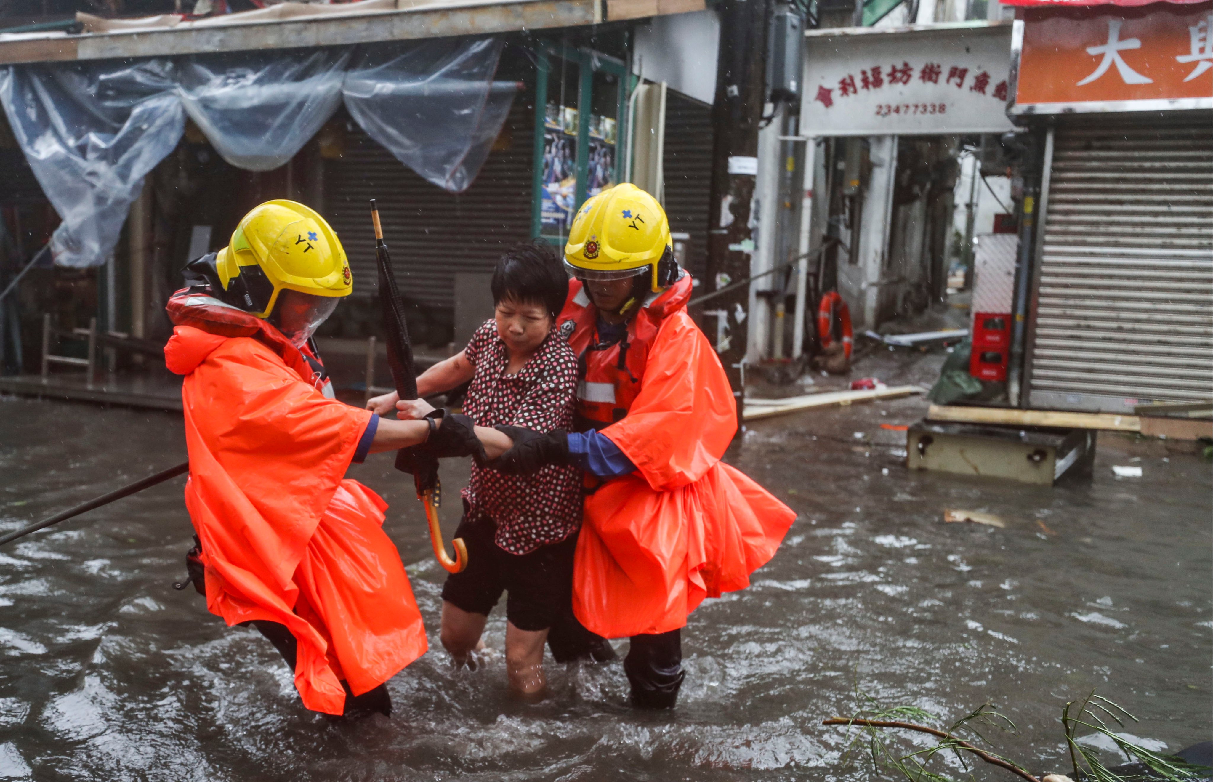 Firefighters help a woman through flooded streets on September 16, 2018, after strong winds and waves lashed Hong Kong when Typhoon Mangkhut made landfall. Photo: Winson Wong