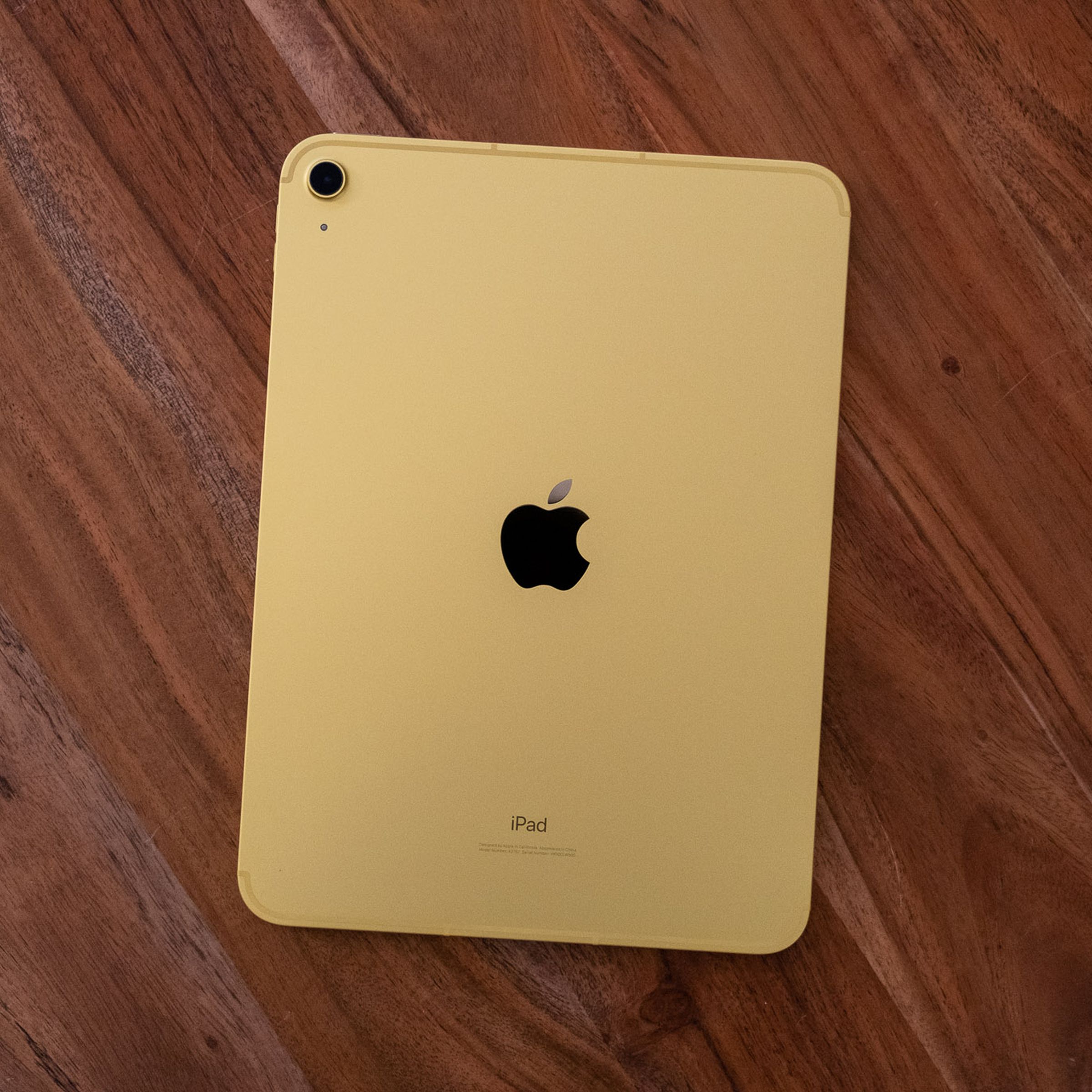 A yellow 10th gen iPad face down on a wooden table, seen from above.