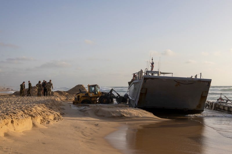 U.S. soldiers look on as a digger attempts to extricate a U.S. Army vessel that ran aground at a beach in Israel's coastal city of Ashdod on May 25, 2024.