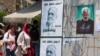 Young women flouting the mandatory Islamic head scarf walk past electoral posters of moderate candidate Masud Pezeshkian (left) and hard-line hopeful Saeed Jalili in Tehran.