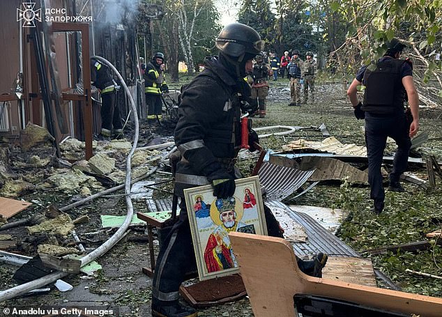 Rescuers pictured working on conducting search and rescue operations on the area with one carrying a painting from the wreckage