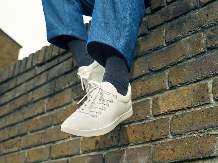 Person's legs dangling over the edge of a brick wall they are sitting on while wearing Allbirds Wool Piper shoes.