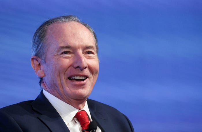 Morgan Stanley CEO James Gorman, wearing a black suit and red tie, smiles in front of a blue backdrop.