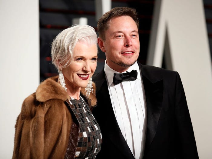 Elon Musk's mother wears a brown coat and stands to the left of Elon Musk, pictured in a tuxedo
