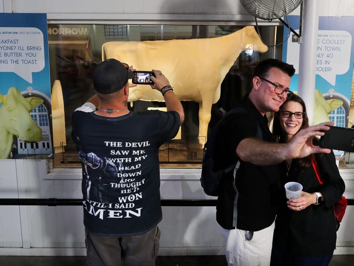 DES MOINES, IOWA - AUGUST 08: People pose for selfies with the famous Butter Cow, made using 600 pounds of low-moisture, pure cream butter, during the Iowa State Fair August 08, 2019 in Des Moines, Iowa.
