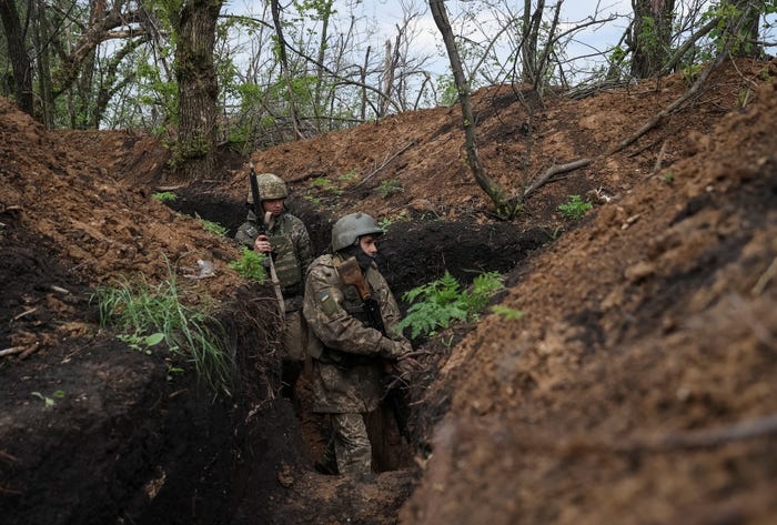 Two Ukrainian soldiers wearing combat gear walk at a fork in a trench