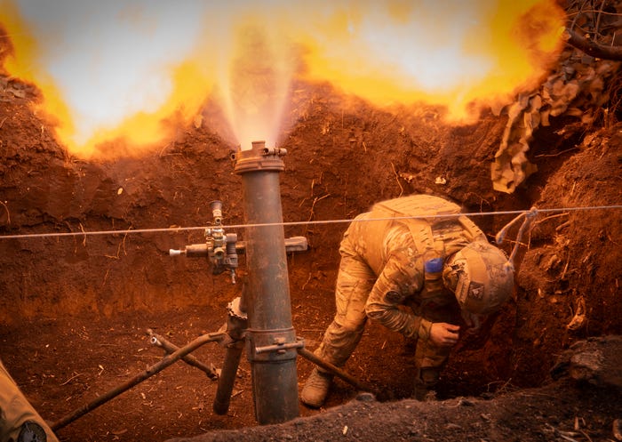 A Ukrainian serviceman crouches over beside a firing 122m mortar