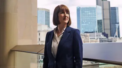Chancellor Rachel Reeves with the City of London skyline behind her and an overcast sky