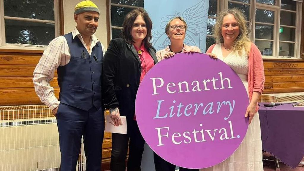 Rhian Elizabeth with three other people at the Penarth Literary Festival, holding a banner with the event's name