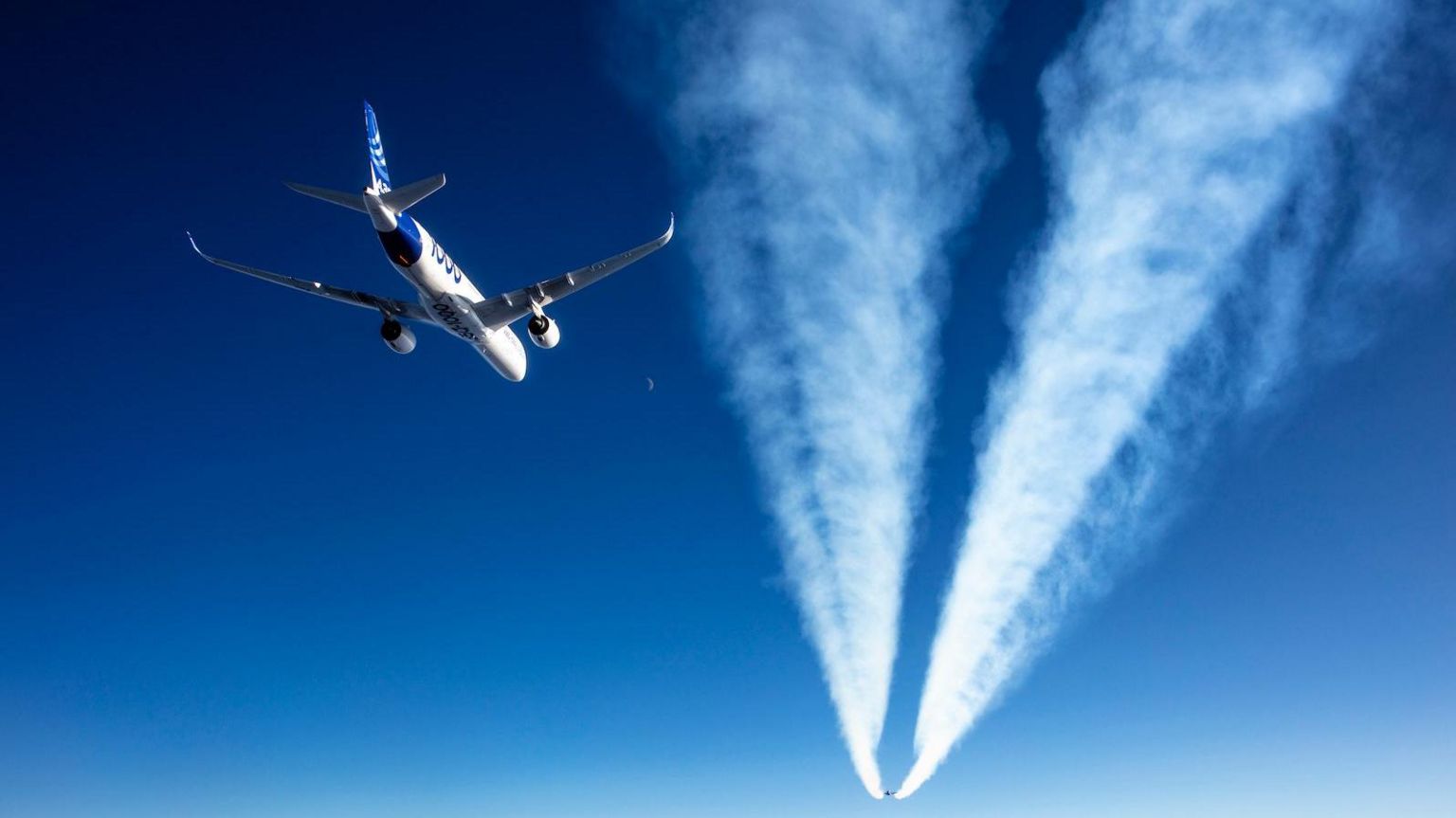 An Airbus A350 flying behind the contrail of another jet in blue skies