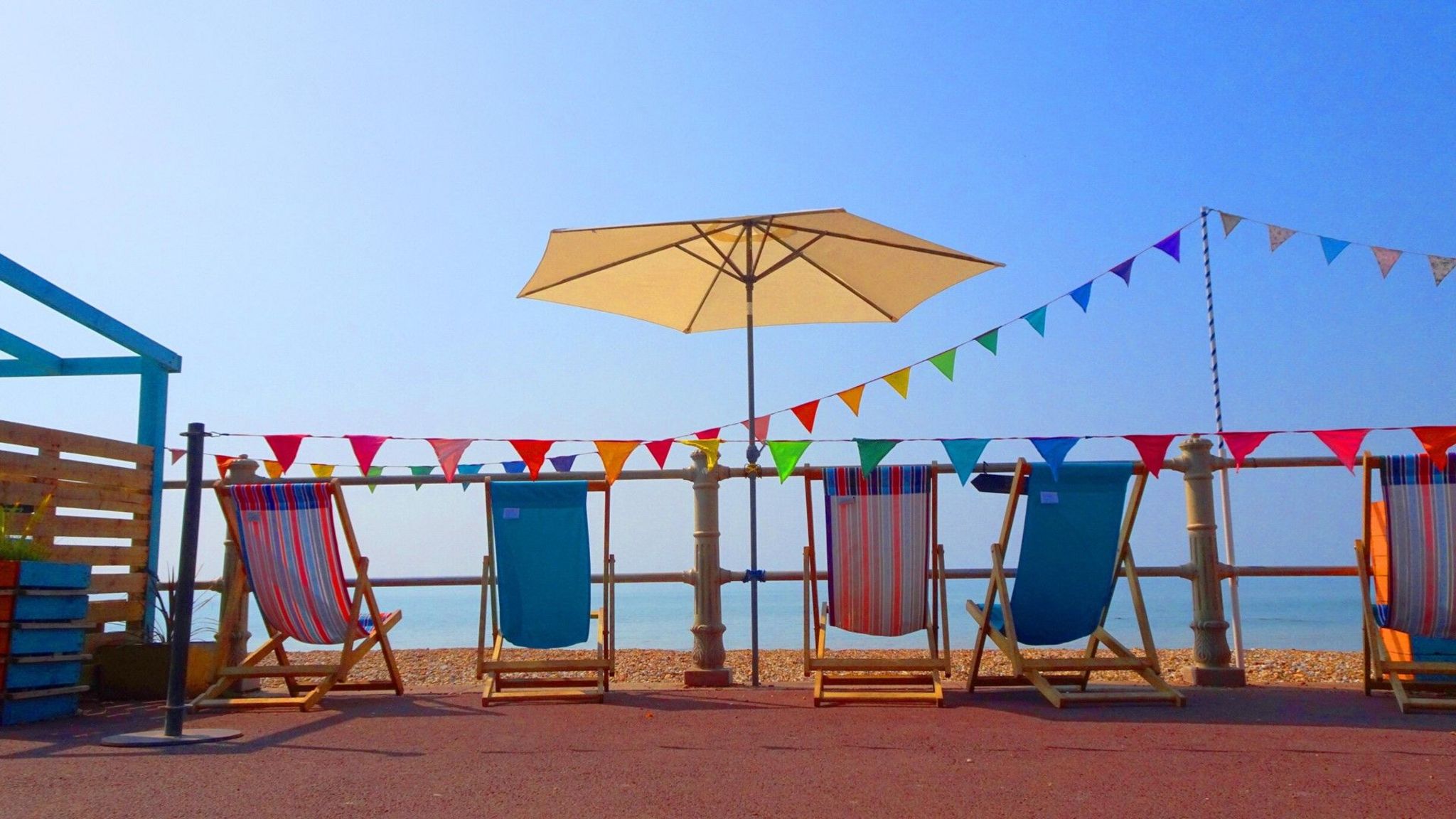 Deckchairs, bunting and a parasol on a seafront with a bright blue sky overhead