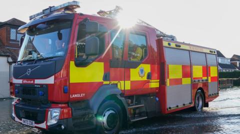 A fire engine, with the sun shining just above it. It is marked with the Berkshire fire service logo