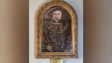 King Henry VIII painting with a gold frame and a gold plaque describing the painting 
