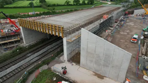 The Carol Green railway bridge shown during construction, it is a concrete structure flanked with scaffolding, cranes and other construction equipment can be seen either side