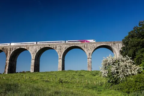 PA Dublin to Belfast train travelling on raised railway bridge with arched columns with green fields underneath