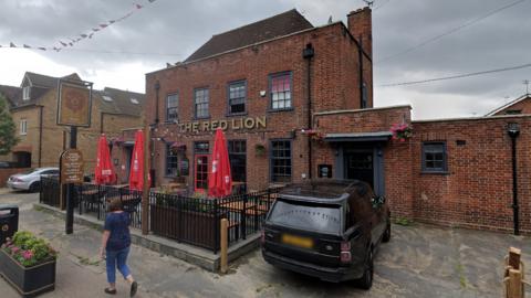 The outside of the Red Lion pub, a large brick building with a beer garden 
