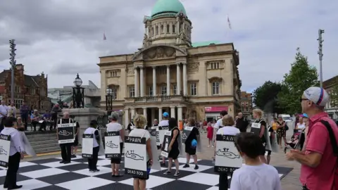 Human chess players on a chess board in front of Hull City Hall