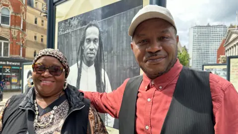 Mr Zepheniah's brother and sister stand in front of a picture of their brother on a street