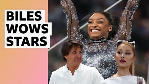 Simone Biles with her hands in the air and a huge smile on her face accompanied by Tom Cruise and Ariana Grande