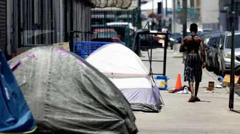 Tents line a street in California as a man without a shirt passes by 