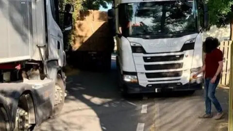 A lorry pulled to the side of a narrow road while an oncoming HGV is moving past