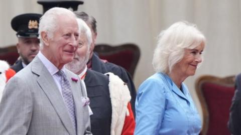 King Charles III and Queen Camilla walk beside a parade of dignitaries