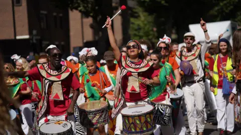 People carrying drums wearing brightly coloured outfits