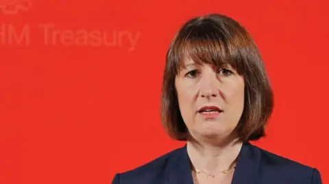 Chancellor Rachel Reeves against a bright red backdrop, with a neutral or slightly negative facial expression