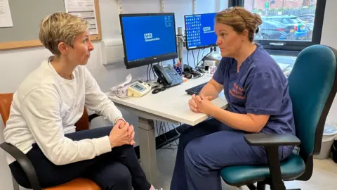 BBC Laura Gelder-Robertson sitting at a desk speaking to a practitioner at Berkeley Place Surgery