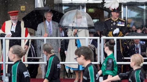 King Charles and Queen Camilla hold umbrellas as a troop of beaver scouts parade past.