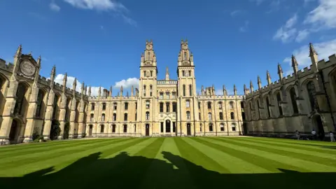 EstherJ The sun shines on an Oxford college sandstone building surrounding a grass quadrangle with blue skies behind