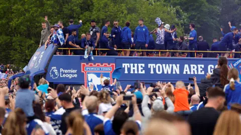 Reuters Fans greet Ipswich Town players, who are stood atop a blue victory bus