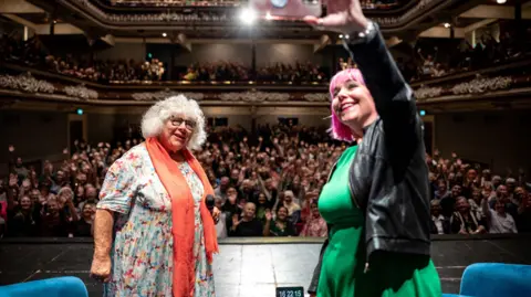 Miriam Margolyes posing for a selfie with audience behind her