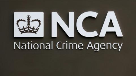 A National Crime Agency sign, with the organisation's name in bold white letters with a crown logo on a black background