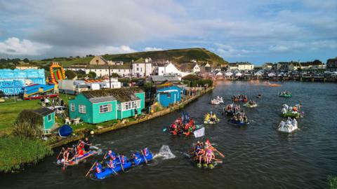 People in fancy dress and homemade rafts drifting down a river