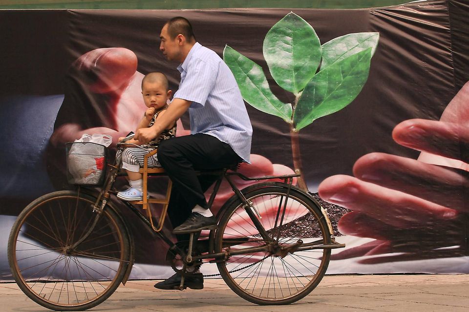 Ein Mann mit Kleinkind radelt an einem Plakat in China vorbei