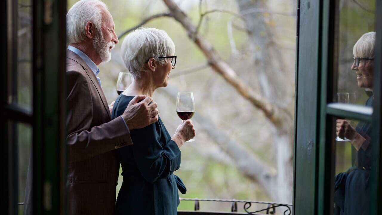 Mature couple drinking from wine glasses on a balcony.