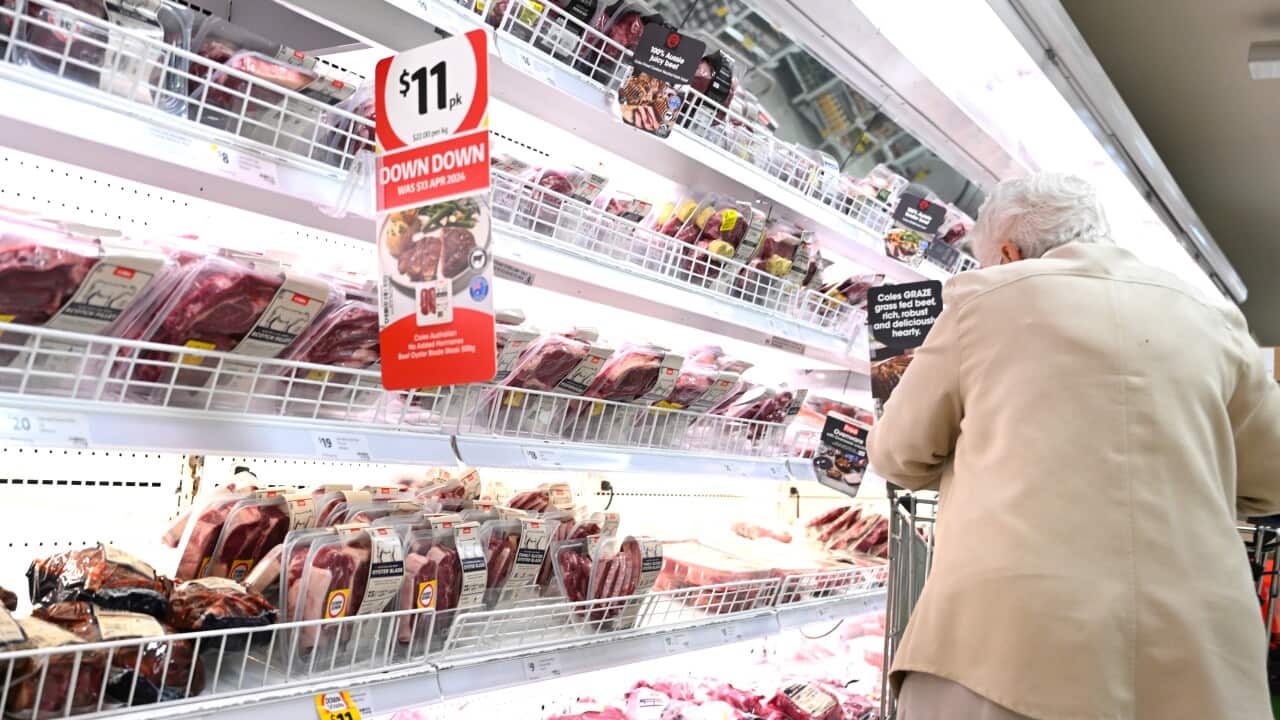 An elderly woman with a shopping trolley looking at the meat section at a Coles supermarket 