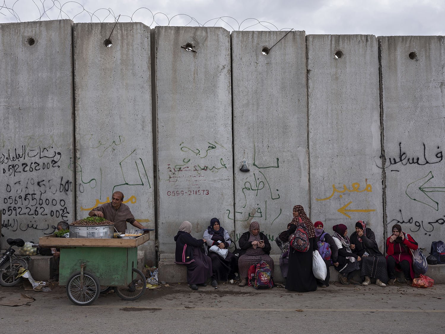  Palestinian women sit on a section of Israel's concrete separation barrier next to a small market at the West Bank city of Qalqilya, March 9, 2022. (AP Photo/Oded Balilty) 
