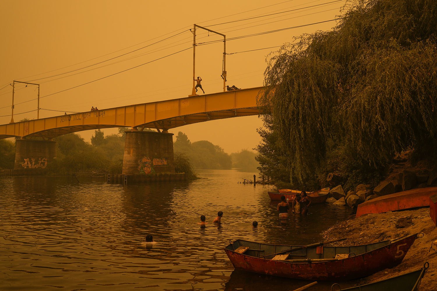  People wade in the Renaico river under a smoked-filled sky caused by wildfires, in Renaico, Chile, Saturday, Feb. 4, 2023. (AP Photo/Matias Delacroix) 