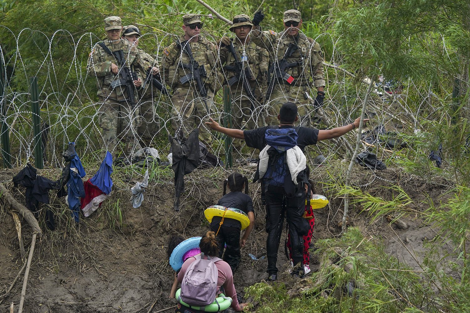  A migrant pleads with Texas National Guards standing behind razor wire on the bank of the Rio Grande, as seen from Matamoros, Mexico, May 11, 2023. (AP Photo/Fernando Llano) 