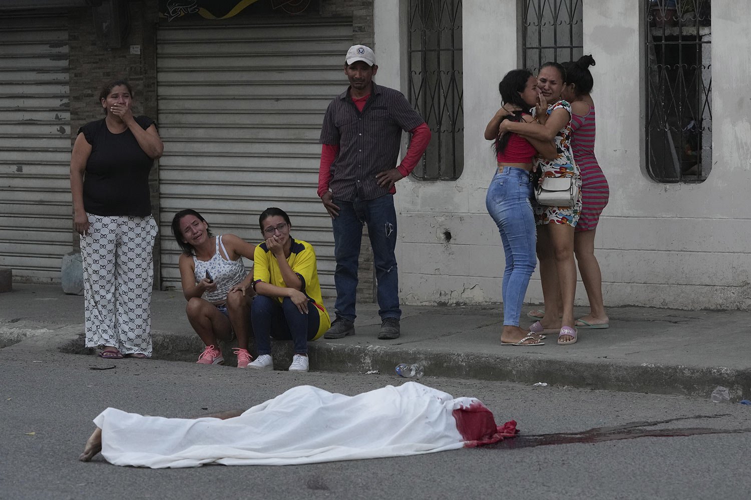  Persons grieve near the body of a man, killed in unknown circumstances, on a street in Duran, Ecuador, July 21, 2023, amid a serious outbreak of violence that authorities attribute to disputes among organized crime groups.  (AP Photo/Dolores Ochoa) 