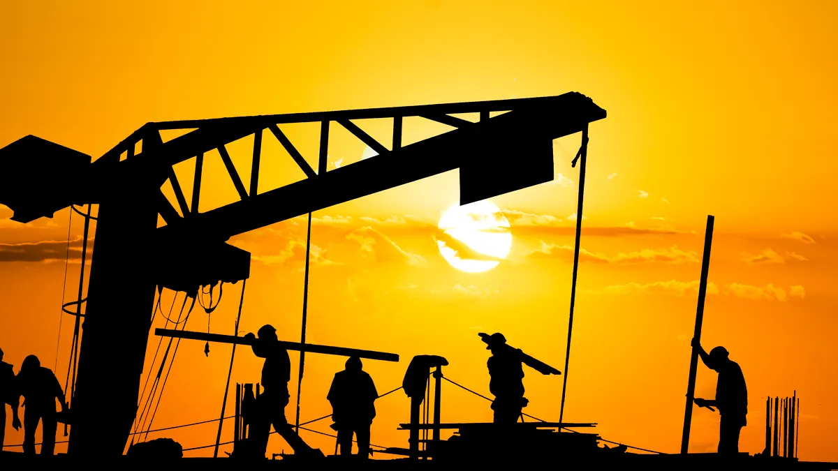 workers toil on a hot construction site with the orange sun in the background
