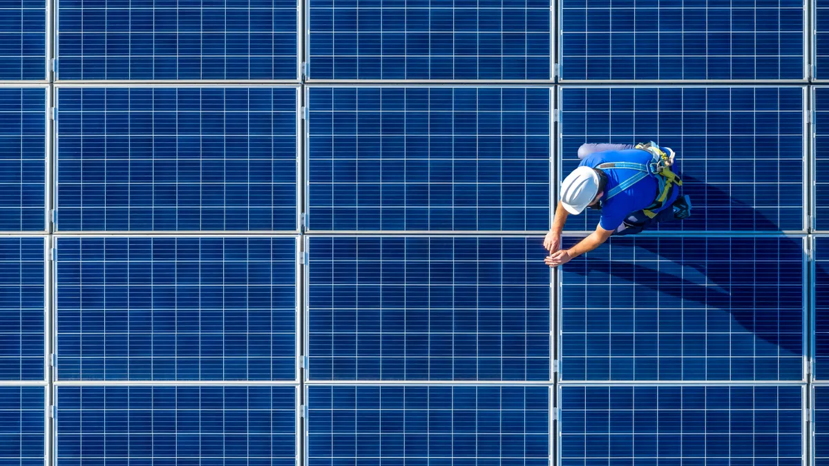Aerial shot of solar panels with a single person in a hard hat working on top of panels